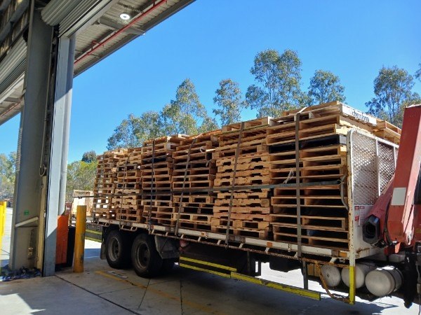 A crane truck loaded with collected pallets at a freight depot