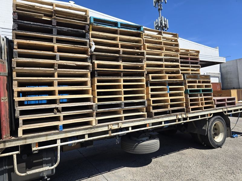 A tray truck stacked with collected pallets outside a warehouse